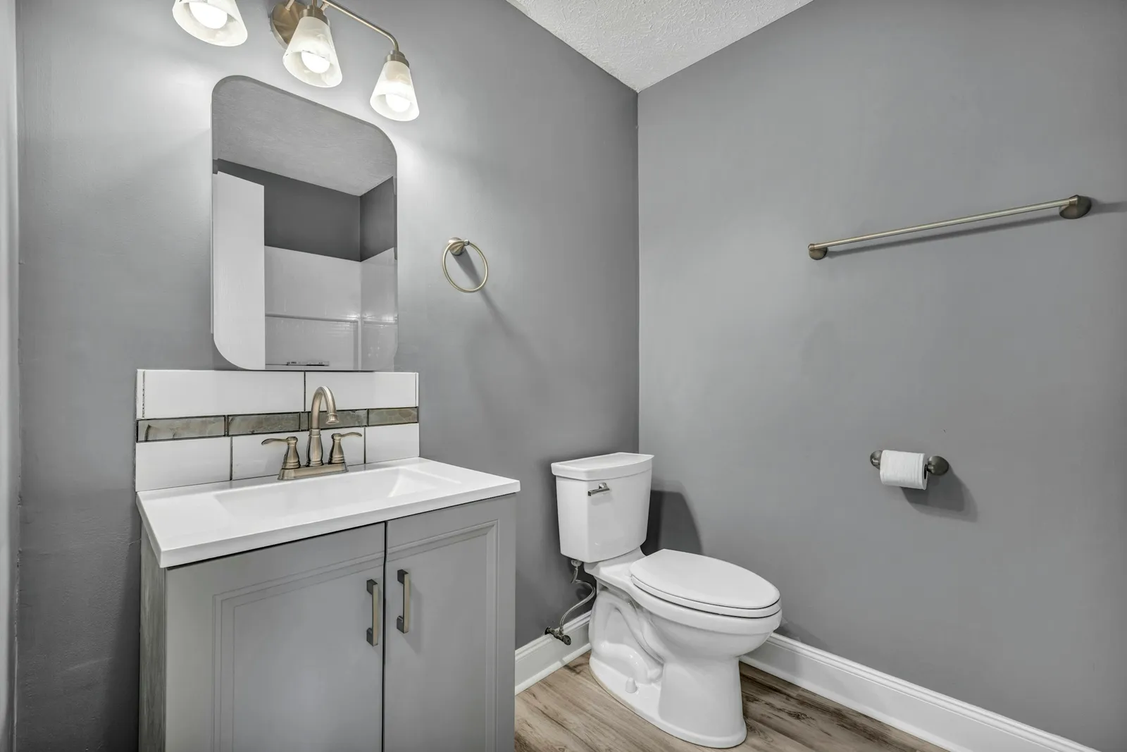 Petite pièce grise avec meuble vasque blanc, miroir rectangulaire, applique à trois lampes et WC