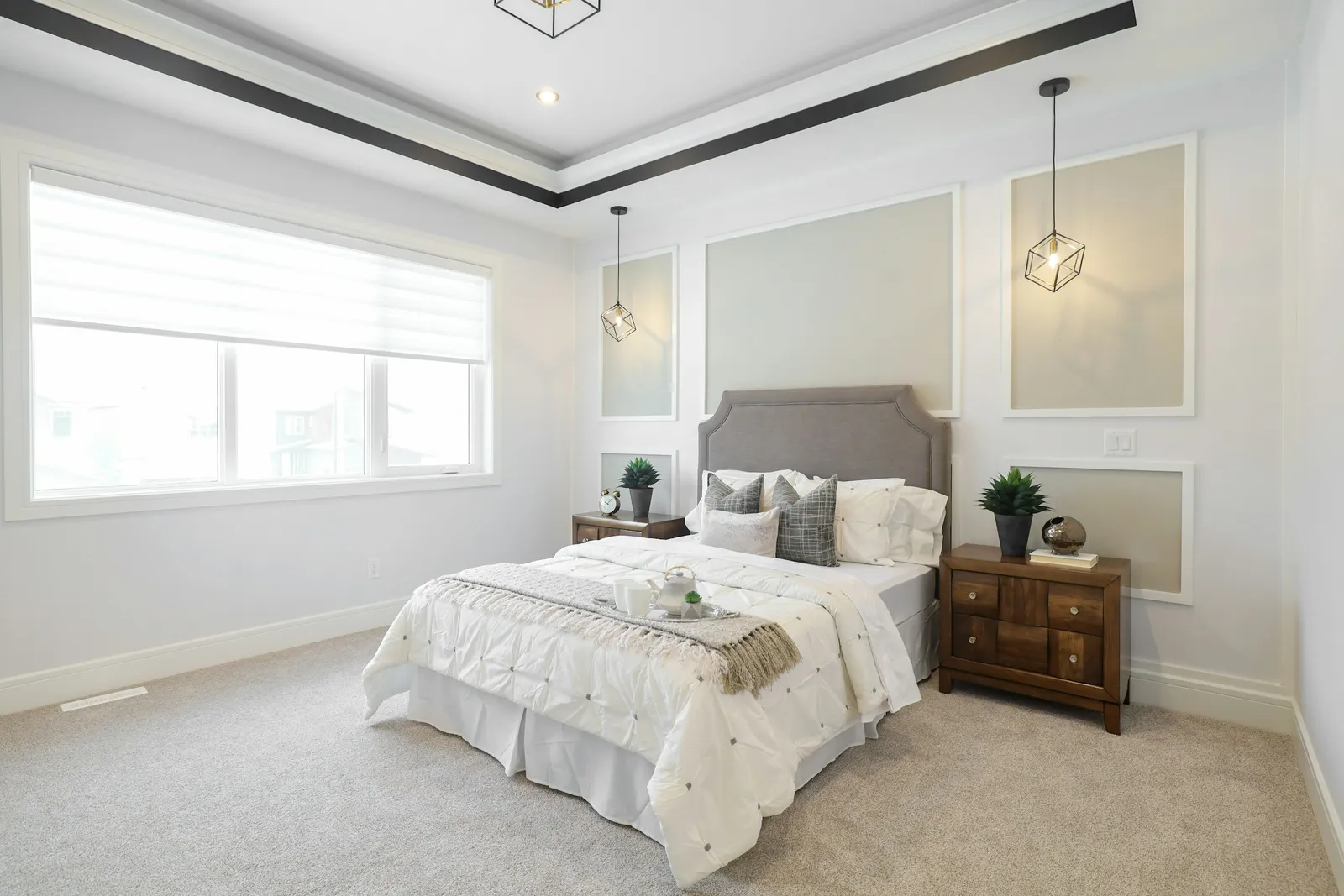 Chambre avec plafond à caisson, moulures murales, tête de lit capitonnée grise, chevets en bois, suspensions cage et moquette grise